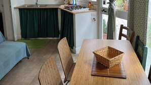 Ett kompakt kök med diskho, spis och ett fönster med gardiner. Det finns också en matplats med ett bord och stolar.