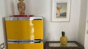 Ett gult kylskåp med en röd topp, en inramad tavla på väggen och en ananas på ett flätat skåp.