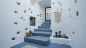 Una escalera con paredes blancas y peldaños azules, rodeada de piedras incrustadas y un tapiz de macramé.
