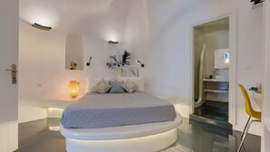 Un dormitorio moderno con una cama ubicada en una plataforma circular, una lámpara de noche y un pequeño estante con adornos.