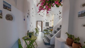 Un pasillo estrecho con un área de comedor que incluye una mesa y sillas verdes, un sofá gris y plantas en macetas.