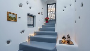 Una escalera con paredes blancas, un cuadro enmarcado, una cortina de encaje y una planta en maceta.