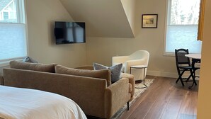 Quarto com cama grande, sofá, televisão e área de refeições com mesa e cadeiras.