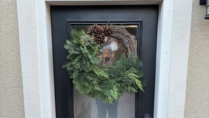 Uma porta preta com uma grinalda, um cadeado numérico e plantas em vasos de cada lado.