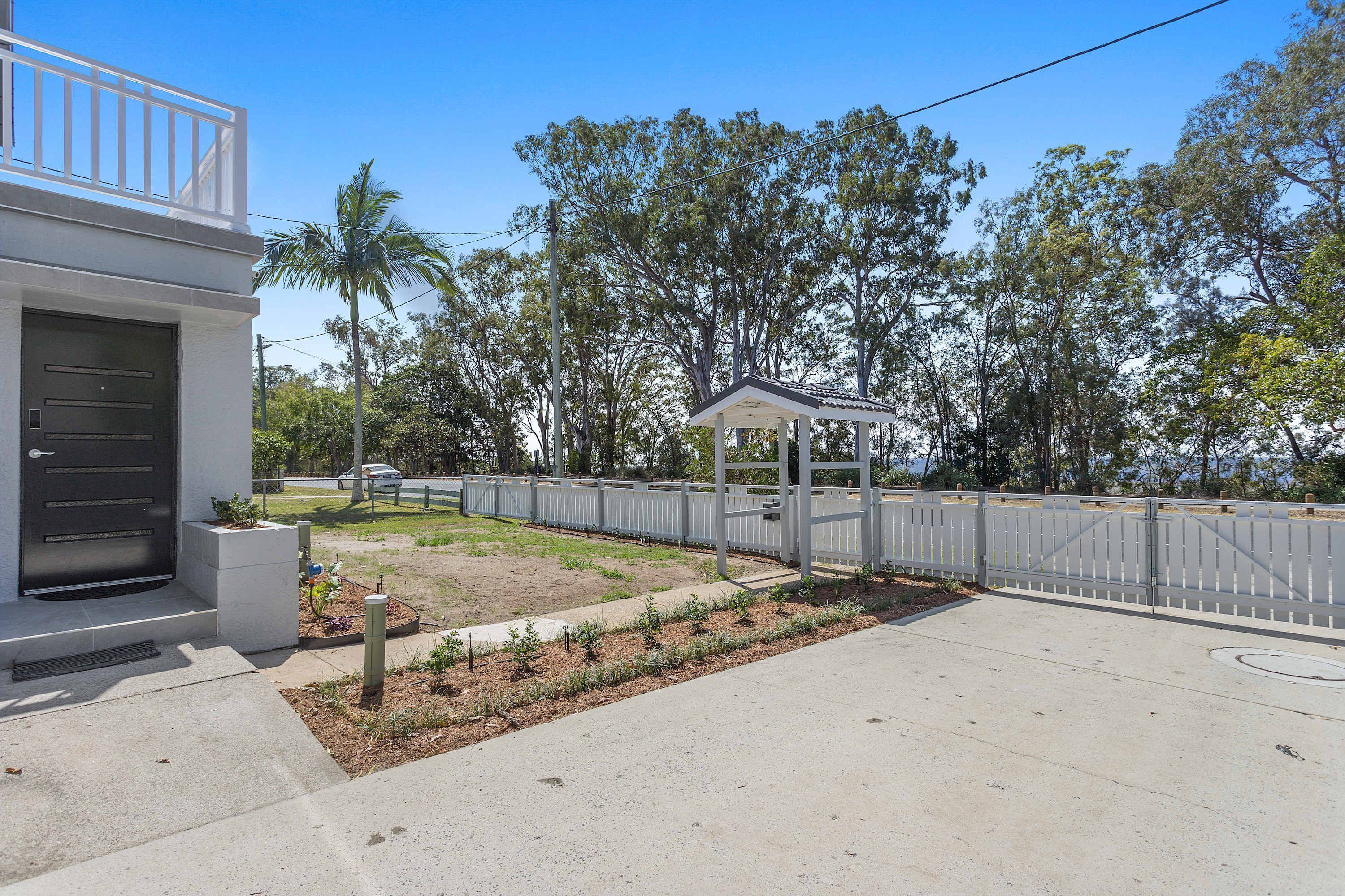 A modern building with a gated entrance, a small garden area, and a clear sky.