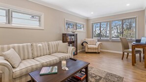 A living room with a sofa, armchairs, a coffee table, a bookshelf, and a dining table. - Metawisebnb Waterfront 3BR Coastal Escape (Deception Bay)