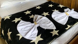 Ein Bett mit schwarzer Bettdecke, verziert mit weißen Sternen, zwei weiße Handtücher, die zu Schleifen gebunden sind, und ein Holzkopfende mit aufwendigen Schnitzereien.