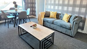 A living room with a grey sofa, a coffee table, and a dining area with chairs and a table. - Bright and Cozy Home Near Hampden Park (Glasgow)