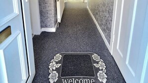 A hallway with a textured wall, a welcome mat, and a door at the end. - Bright and Cozy Home Near Hampden Park (Glasgow)