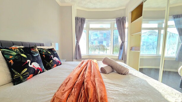 A hotel room with a large bed, a window with curtains, and a view of the outside. - Bright and Cozy Home Near Hampden Park (Glasgow)