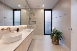 Een moderne badkamer met een grote spiegel, twee wastafels, een douche en een plant in een pot.