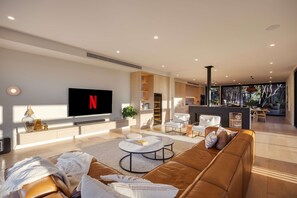A modern living room with a flat-screen TV, leather sofa, and a coffee table. - The Luxe Seabreeze Heated Pool Spa Cinema (Melbourne)