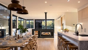 Een moderne keuken met een centraal geplaatste open haard, een houten eettafel en barstoelen.