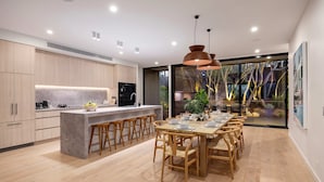 Een moderne keuken met een centraal kookeiland, houten barstoelen en een eettafel voor zes personen.