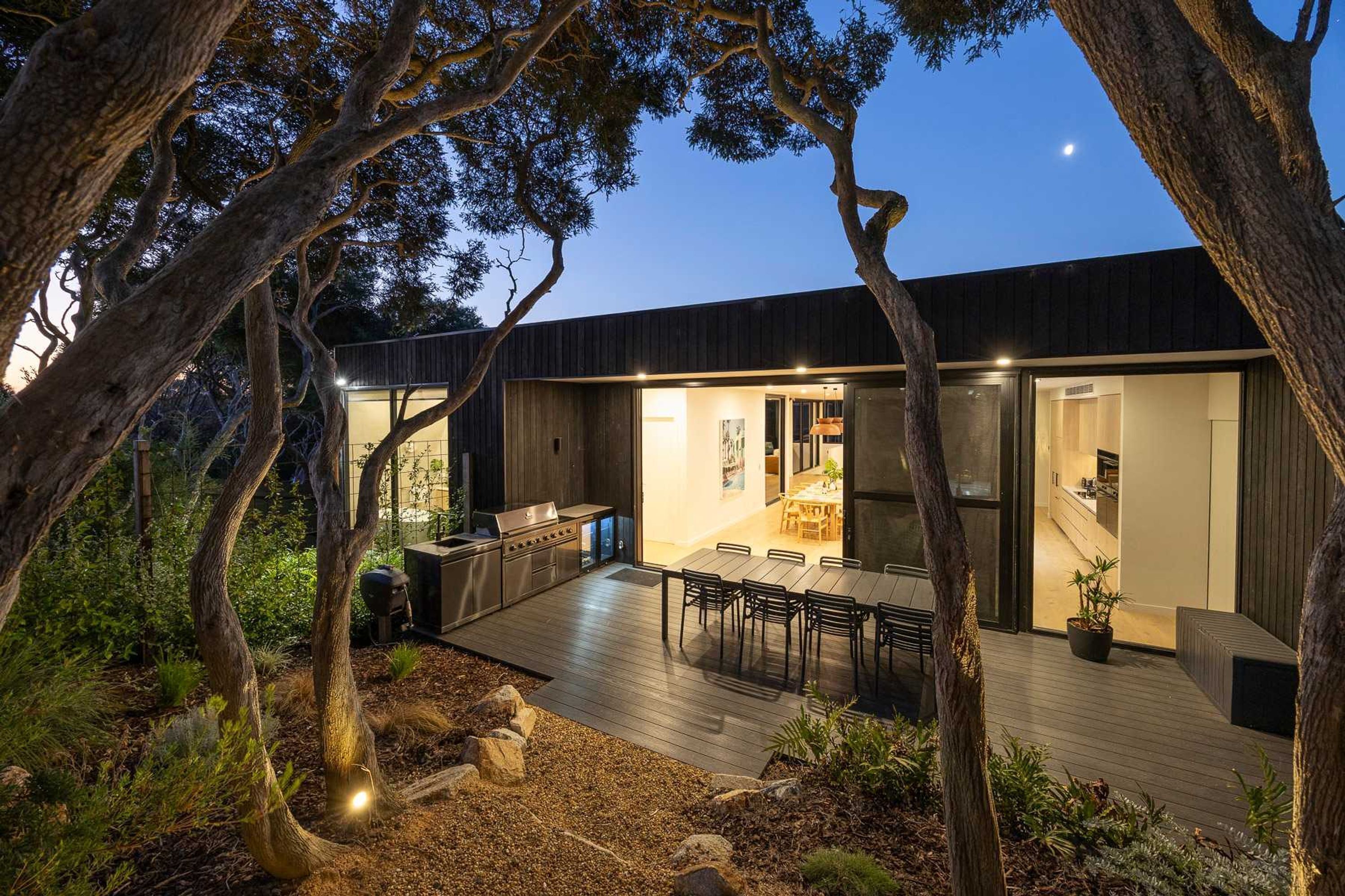 A modern house with a deck, outdoor kitchen, and dining area.