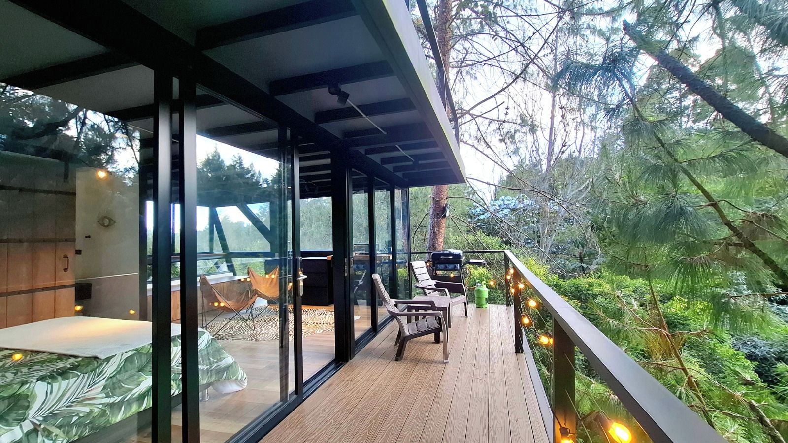 A modern outdoor deck with glass walls, wooden flooring, and outdoor furniture.