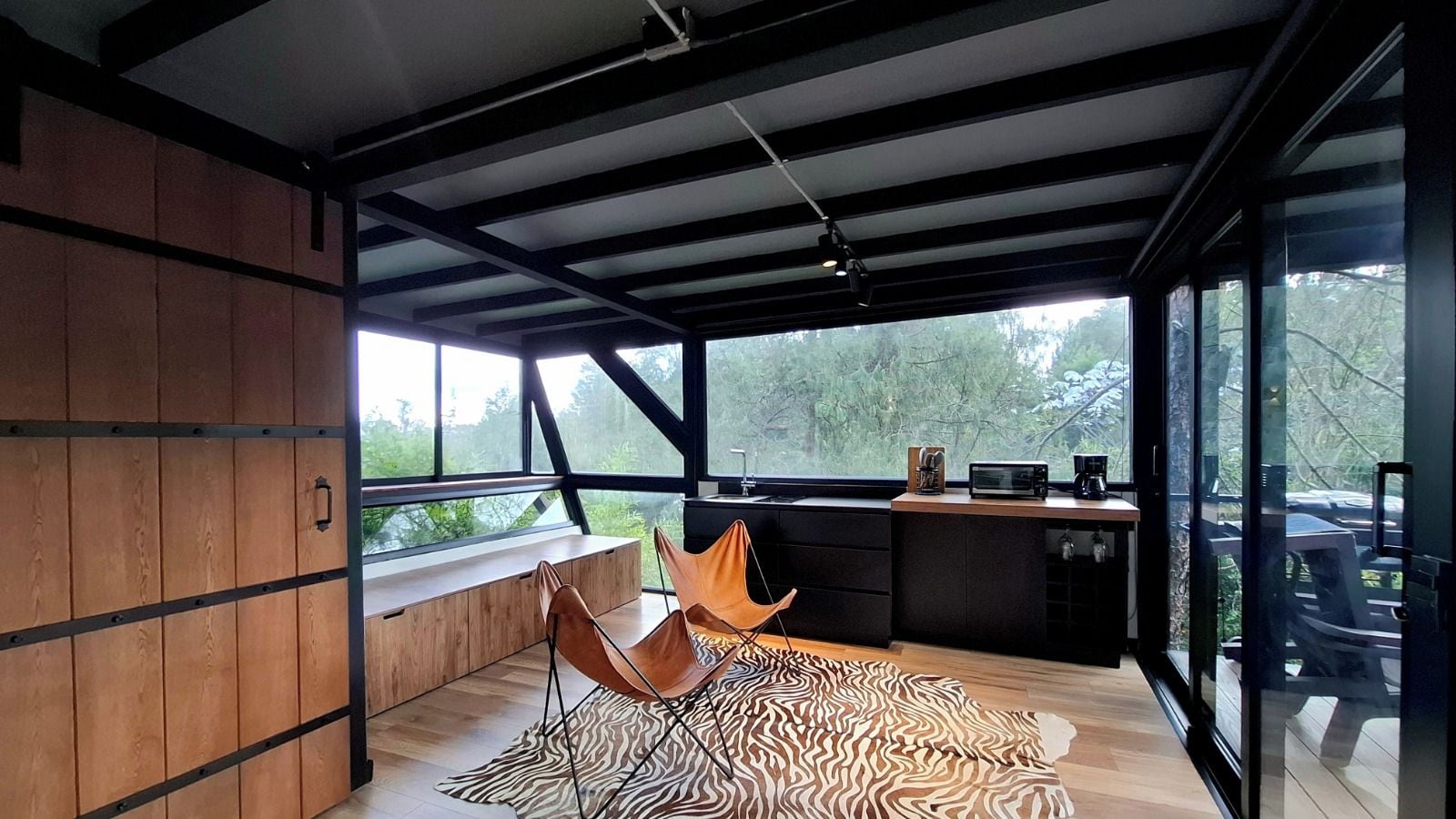 A modern kitchen with a large window, a wooden bench, and a zebra-patterned rug.