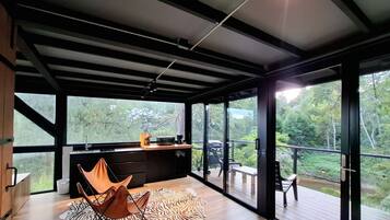 A modern kitchen with a large window, a zebra-patterned rug, and a wooden deck with outdoor furniture.