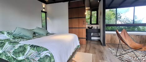 A bedroom with a bed, a chair, a small table, and a window.