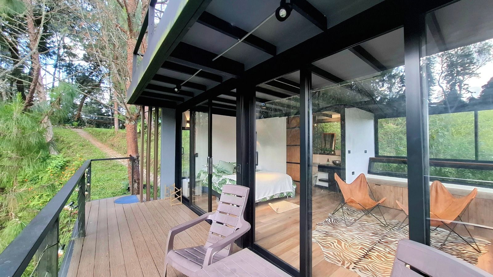 A modern outdoor deck with a wooden floor, glass walls, and a bed with a zebra-patterned rug.