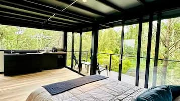 Une chambre moderne avec un grand lit, un bureau et un balcon offrant une vue sur la verdure.