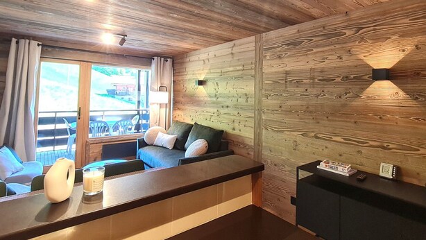 Quarto com painéis de madeira, um sofá, uma mesa pequena e uma janela.