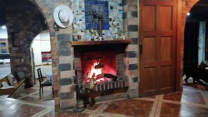 A stone fireplace with a fire, a wooden door, and a tiled floor. - Tranquil Villa Retreat Near Medellin With Private Pool (Guarne)