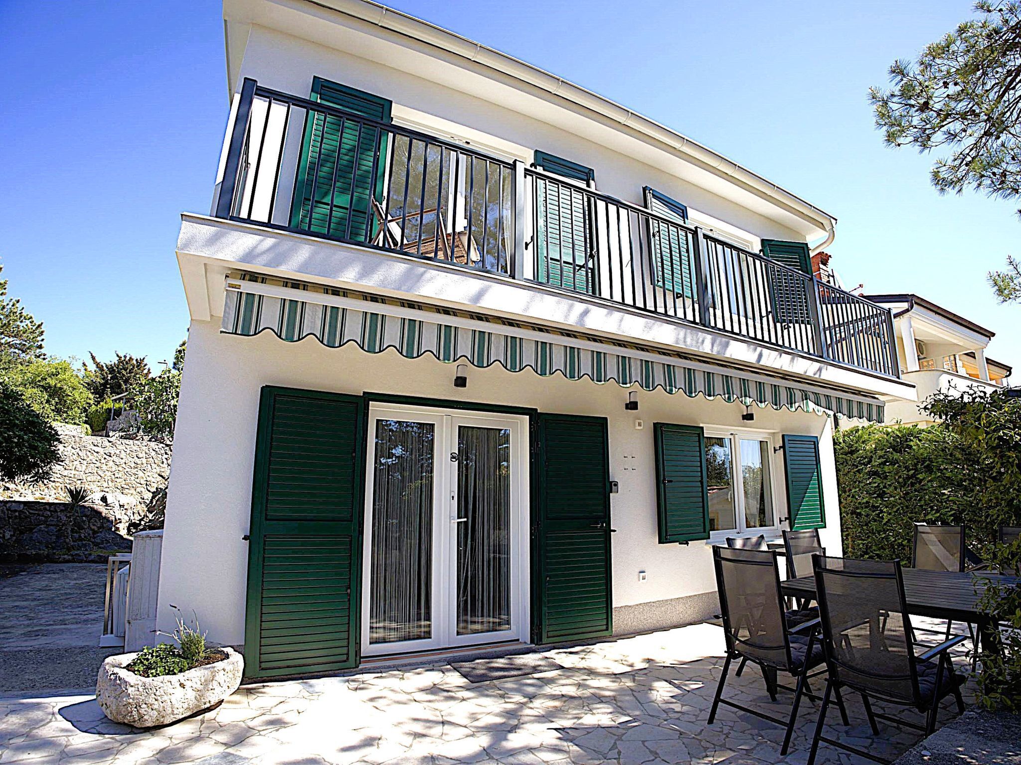 A two-story building with a balcony, a stone-paved patio, and outdoor furniture.