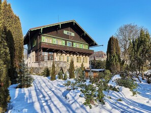A traditional chalet with a wooden facade, multiple windows, and a snow-covered landscape.