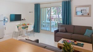 Ein modernes Wohnzimmer mit einer Couch, einem Esstisch mit Stühlen, einem Fernseher und einem Balkon mit Vorhängen.