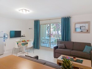 Ein modernes Wohnzimmer mit einer Couch, einem Esstisch mit Stühlen, einem Fernseher und einem Balkon mit Vorhängen.