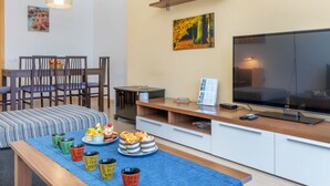 A modern living room with a TV, dining area, and a coffee table with pastries. - Apartment Odisea by Interhome (Lloret de Mar)