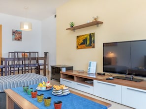 Una sala moderna con televisor, comedor y una mesa de centro con pasteles.