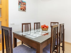 A dining table with chairs, a glass top, and a basket of apples.