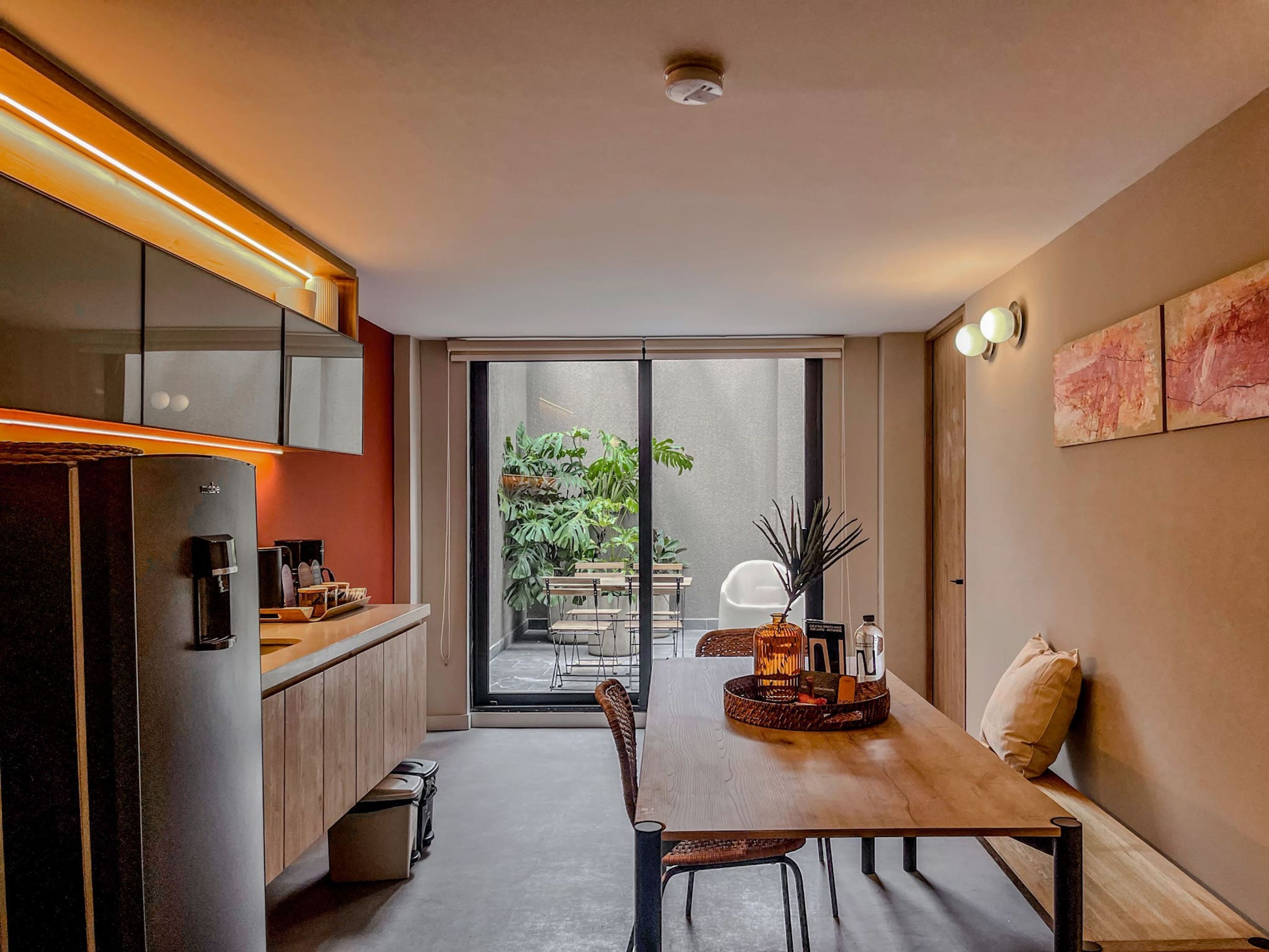 A modern kitchen with a built-in refrigerator, a wooden dining table, and a sliding glass door leading to an outdoor area with a table and chairs.