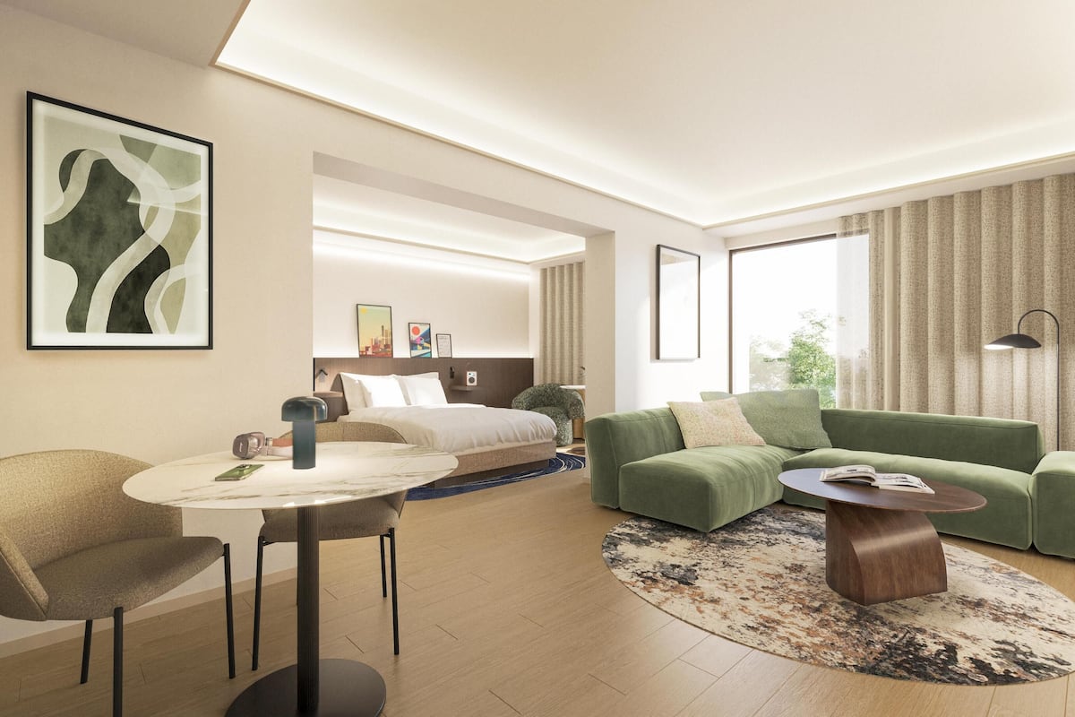 A modern hotel room with a bed, green sofa, armchair, and a round table.