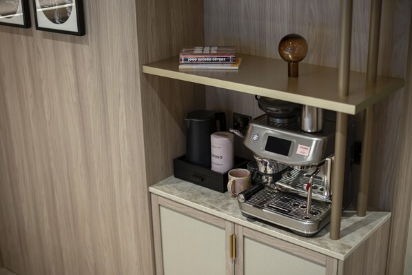Una cafetera sobre una encimera, con un molinillo de café y una taza.