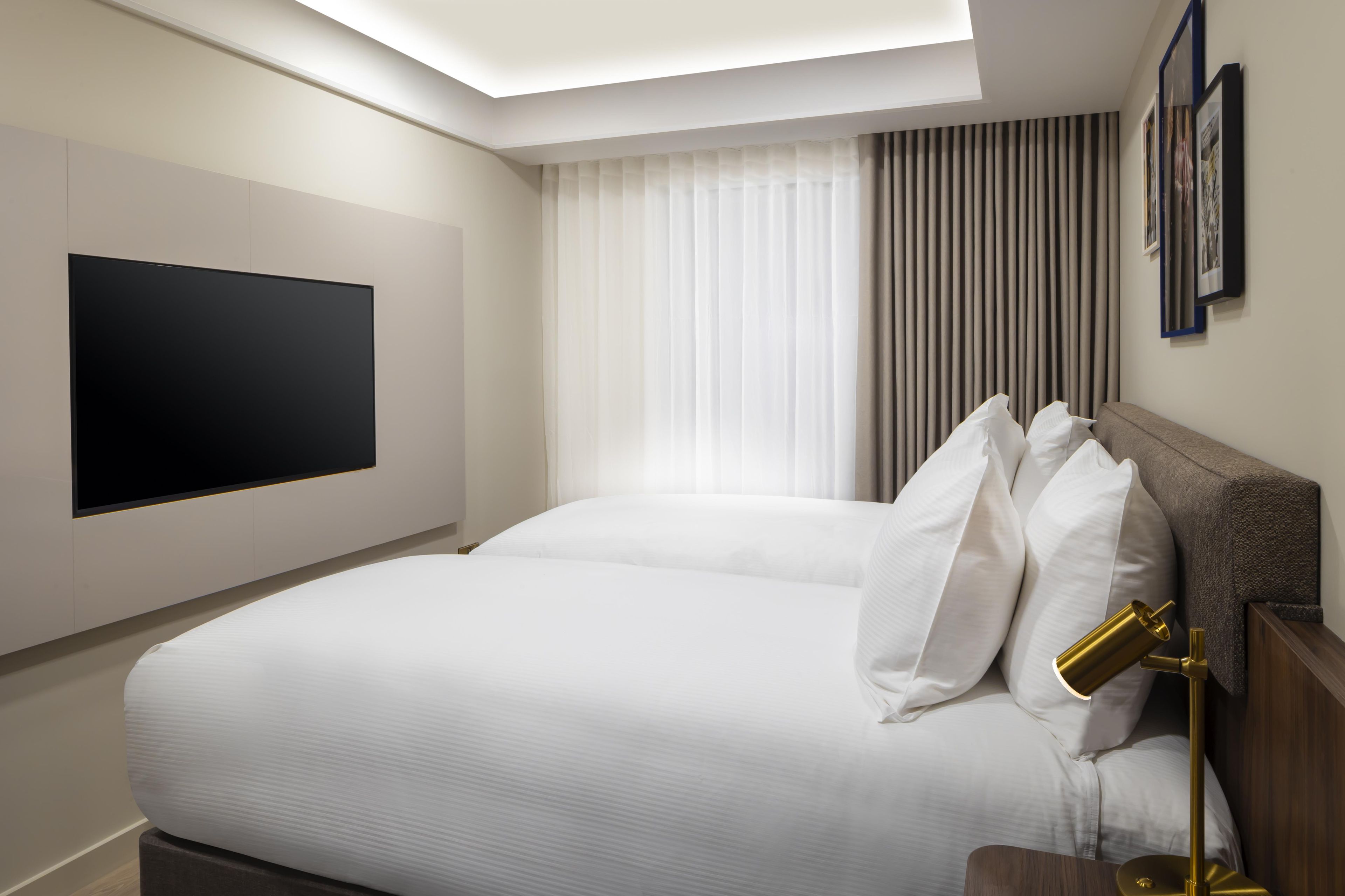 Een moderne hotelkamer met een groot bed, een flatscreen televisie aan de muur, een nachtkastje met een lamp en een raam met gordijnen.