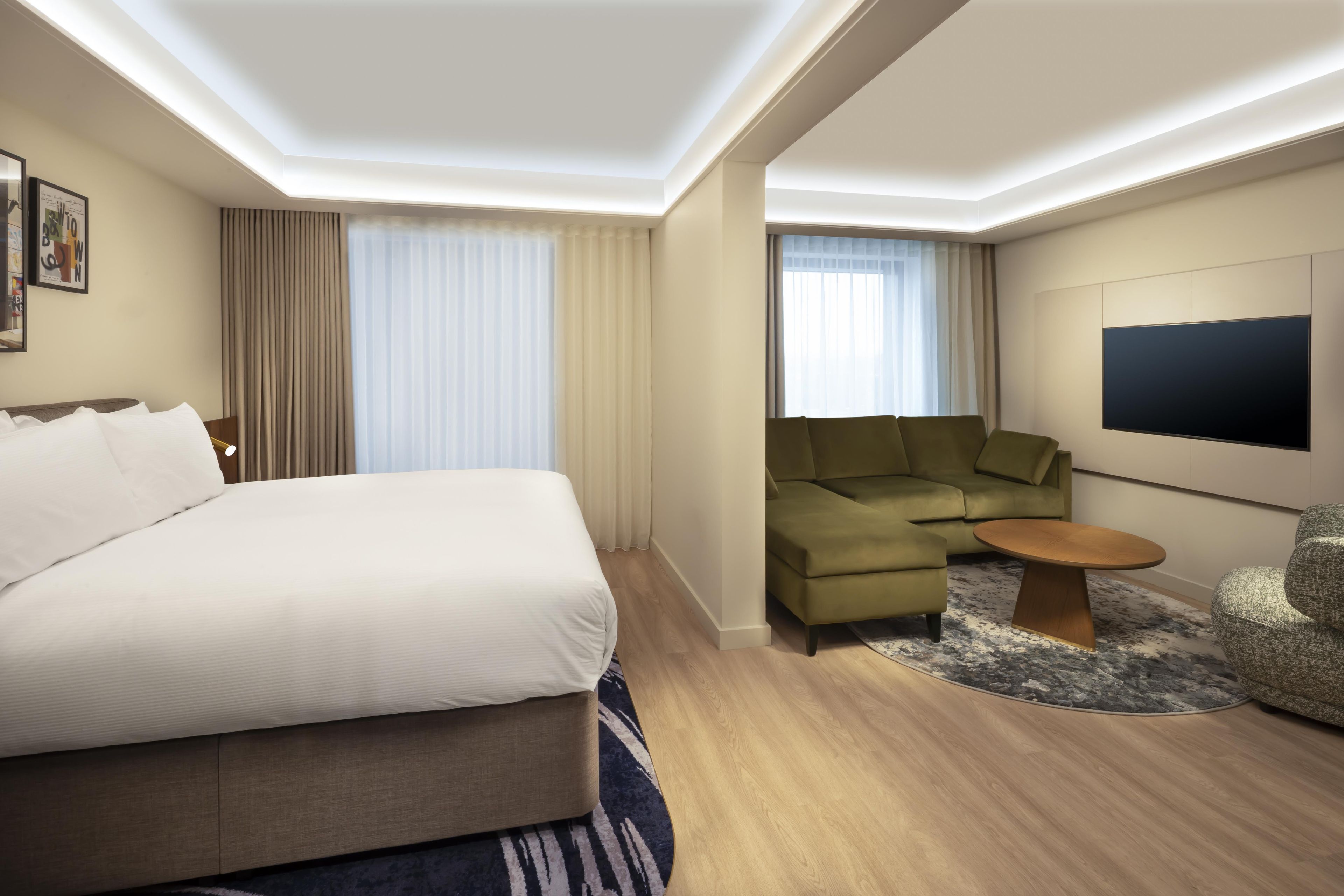 A hotel room with a large bed, a sofa, a small table, and a TV on the wall.