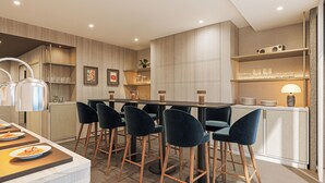 A modern kitchen with a dining area, featuring a wooden table, dark chairs, and a bar counter with stools. - Radisson Blu Medlock Hotel, Manchester (Manchester)