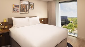 A hotel room with a large bed, a nightstand, a desk lamp, and a window with a view of greenery. - Radisson Blu Medlock Hotel, Manchester (Manchester)