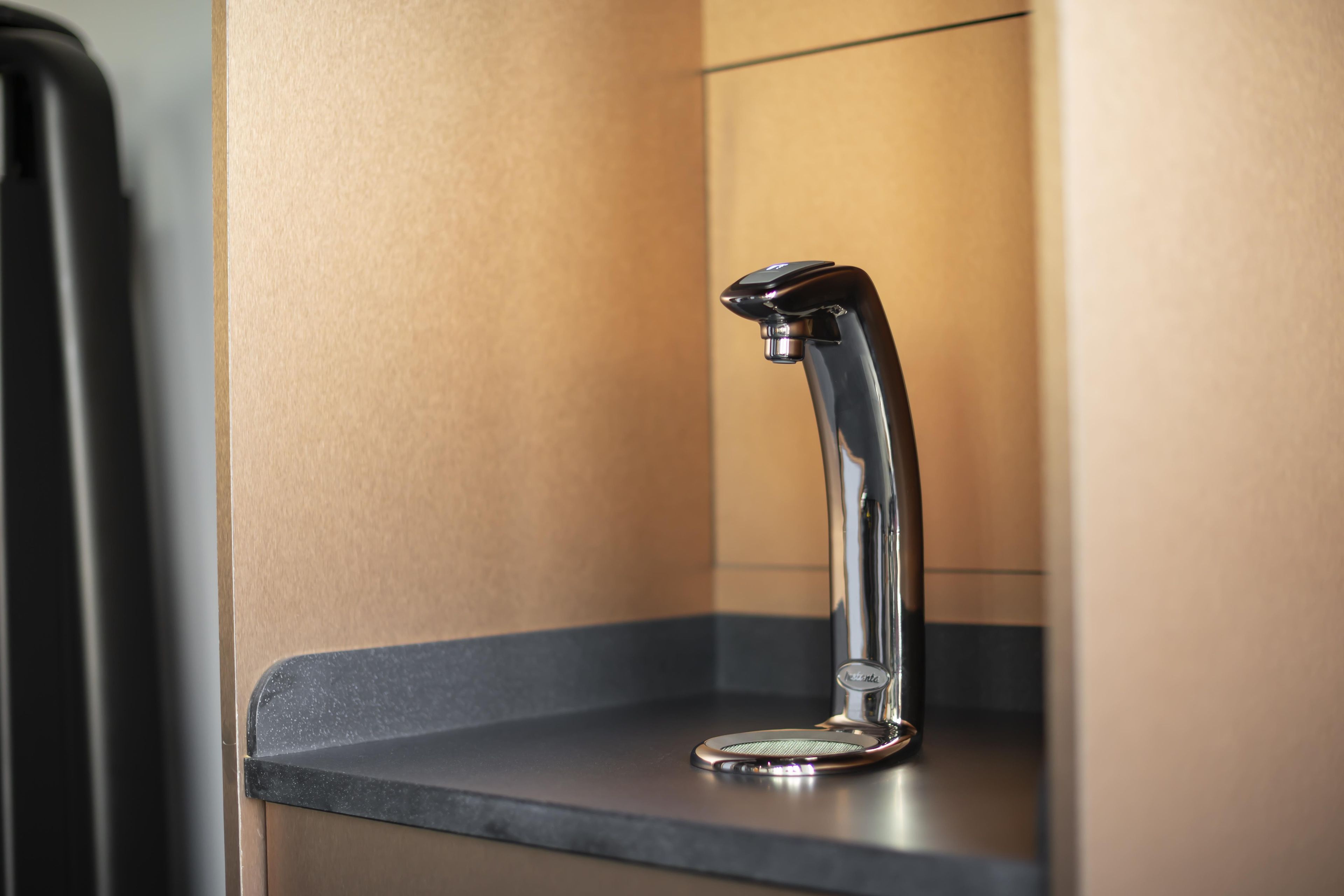 Ein moderner, metallischer Wasserhahn mit einem einzelnen Hebel auf einer dunklen Arbeitsplatte, vermutlich in einem Badezimmer.