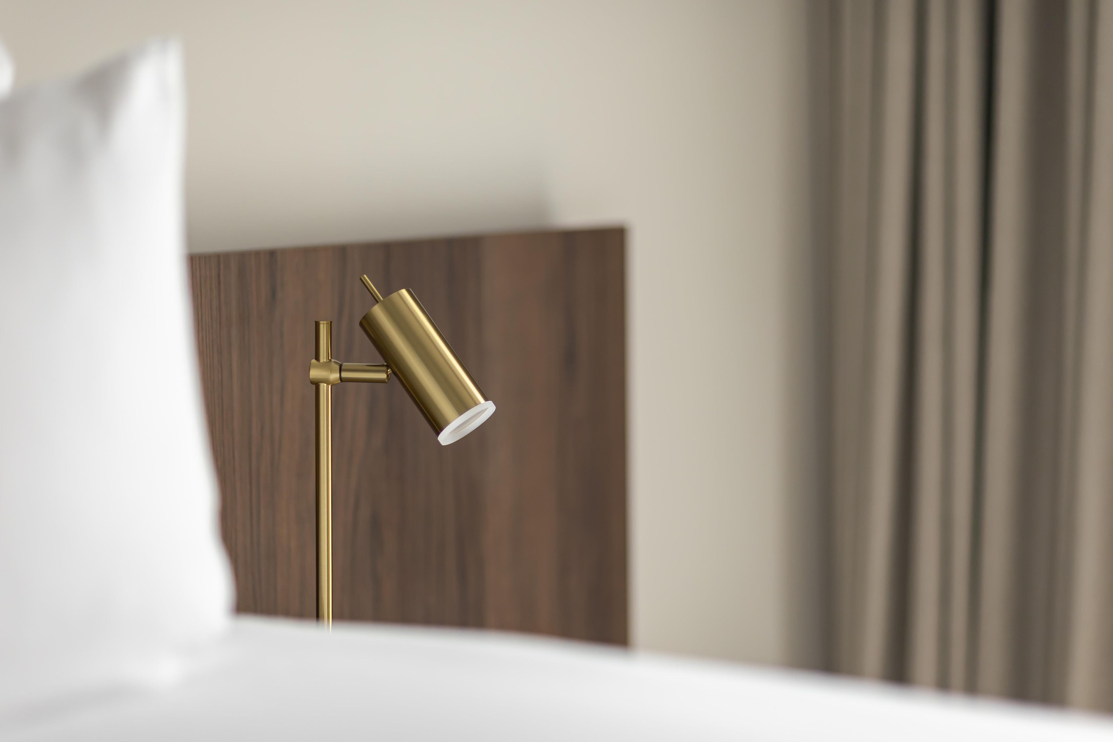 A modern hotel room with a bed, a bedside lamp, and a wooden headboard.