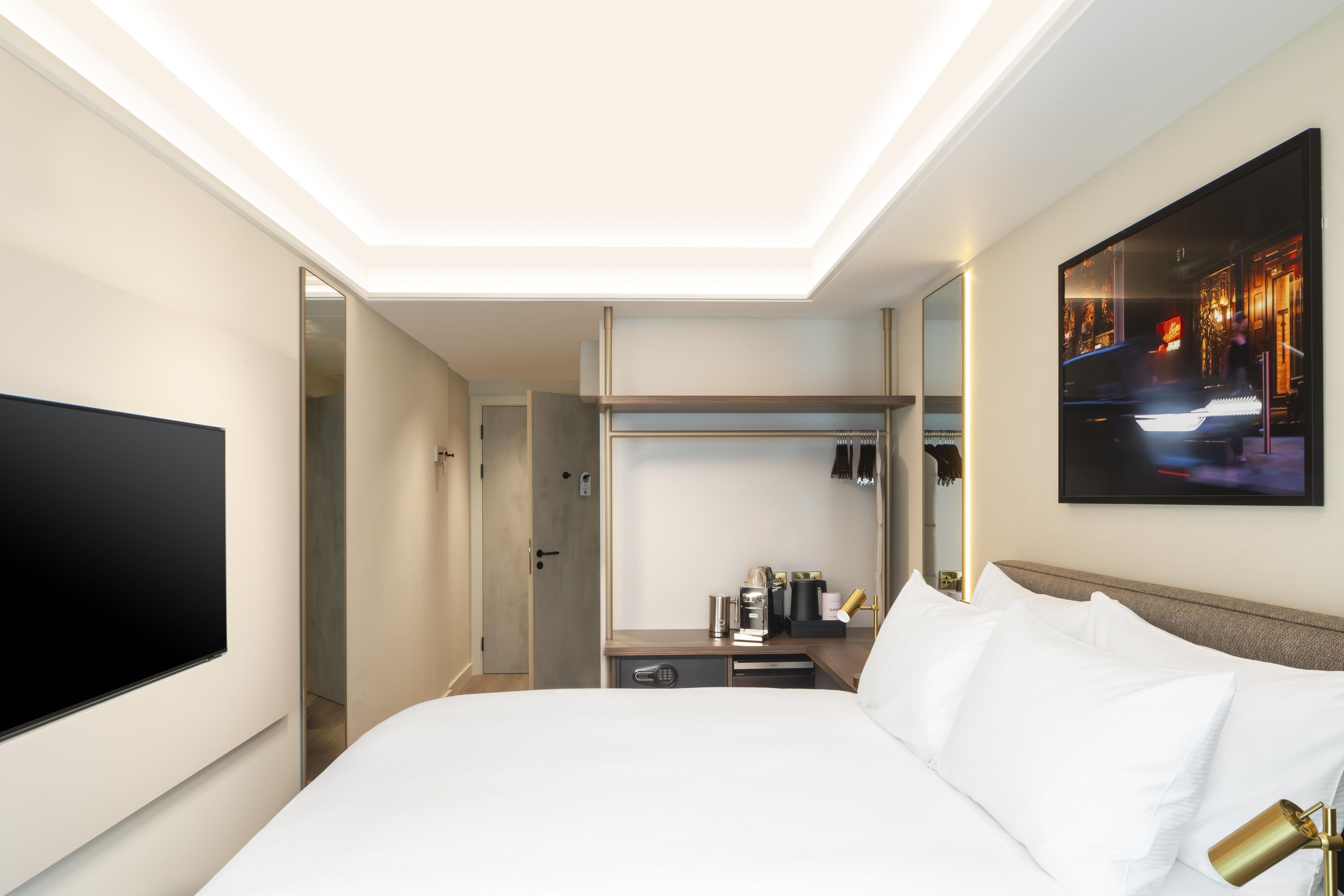 Een hotelkamer met een bed, een flatscreen televisie, een nachtkastje met lamp, een kapstok en een spiegel.