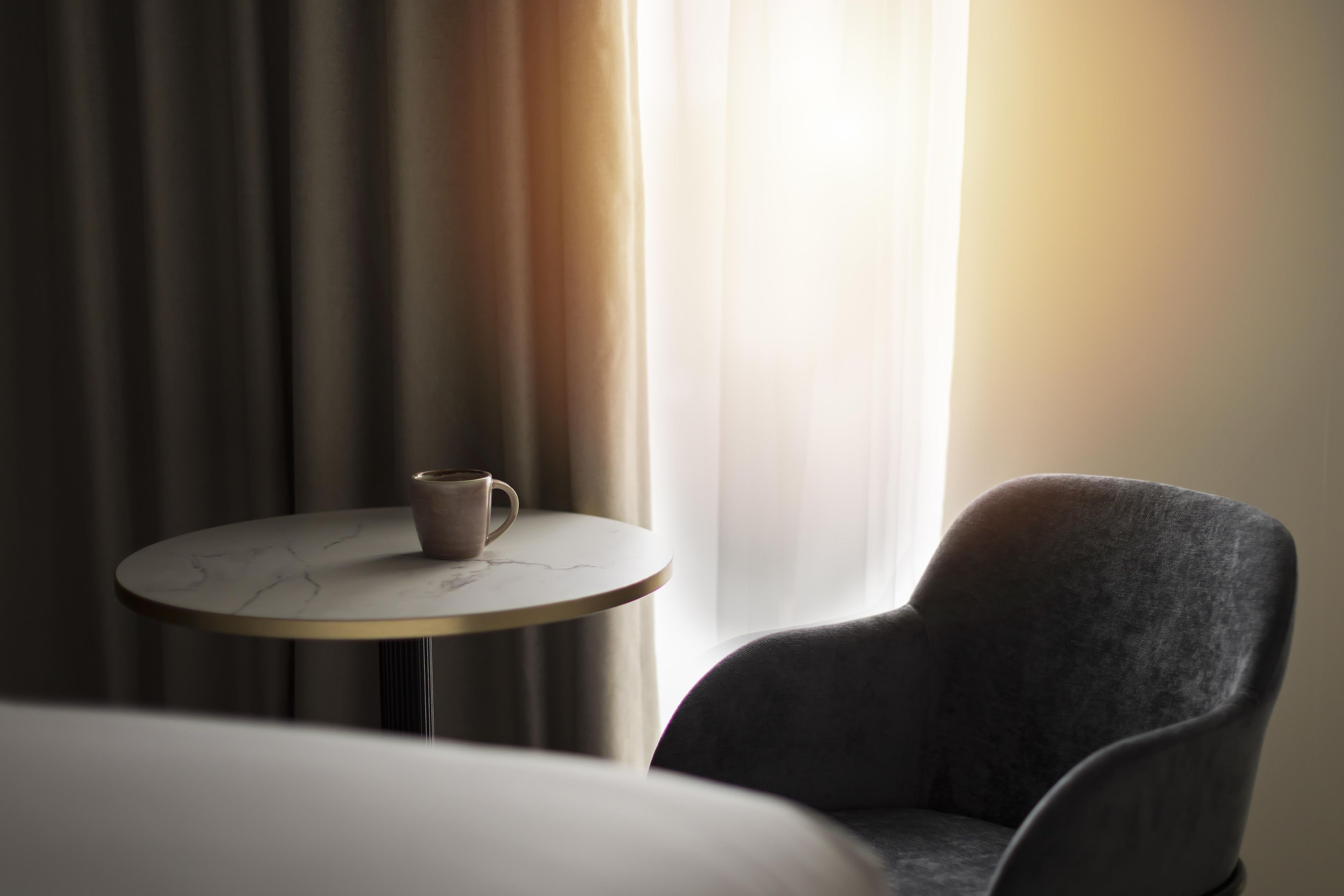 Una habitación con una mesa redonda, una silla individual y una ventana con cortinas.