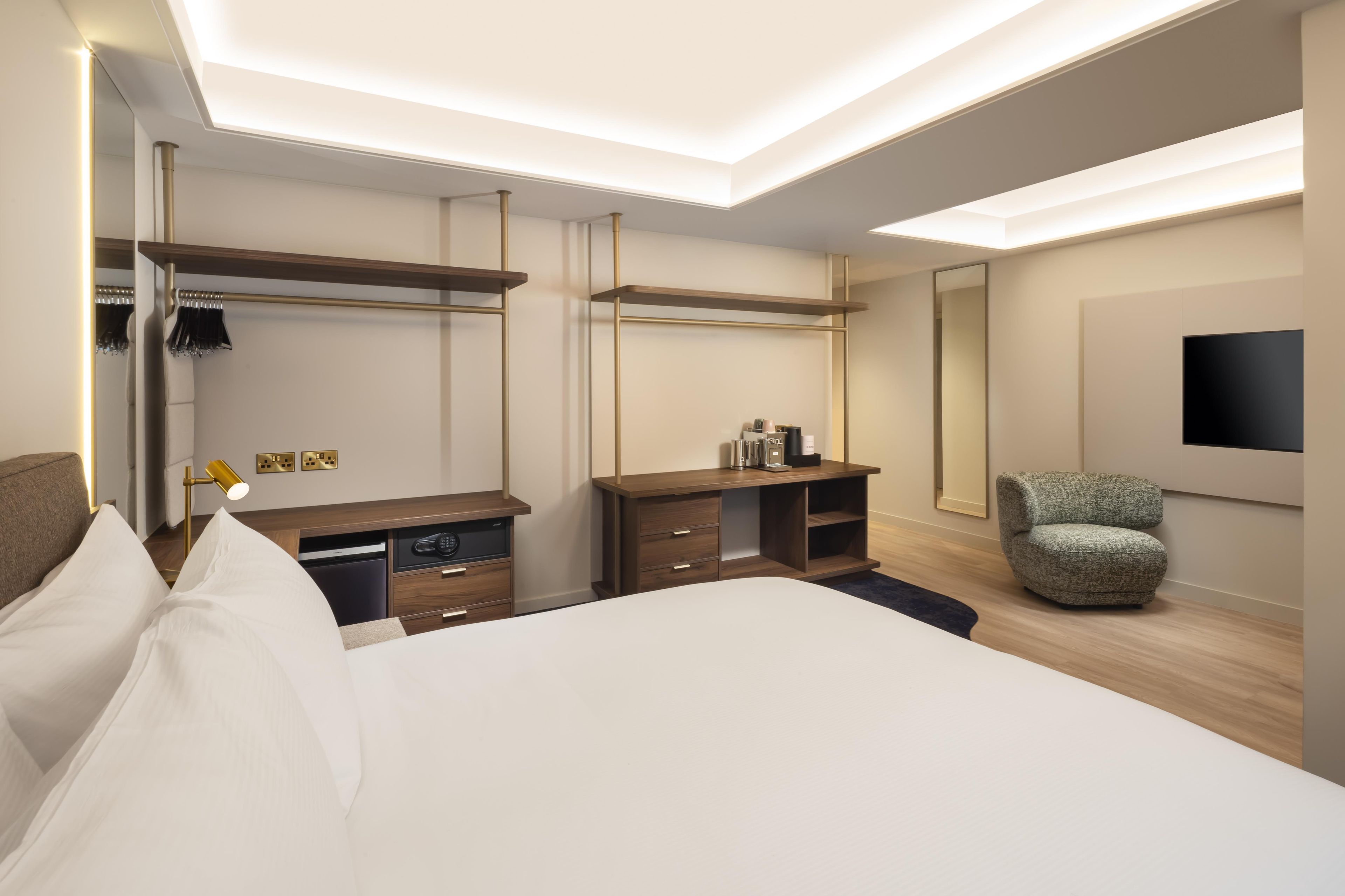 Una habitación de hotel moderna con una cama grande, un escritorio, una silla y un televisor montado en la pared.