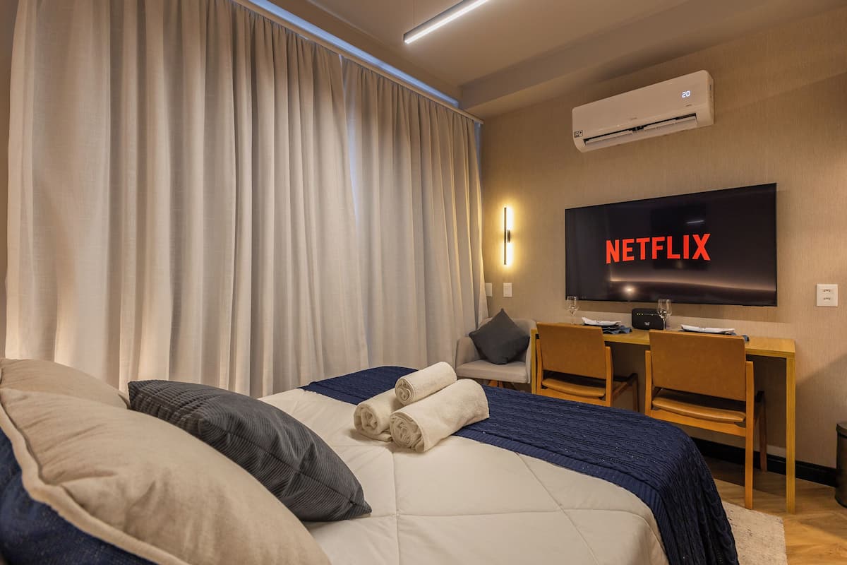 Une chambre d’hôtel équipée d’un lit, d’un bureau, de deux chaises, d’un téléviseur affichant le logo « NETFLIX » et d’un appareil de climatisation.