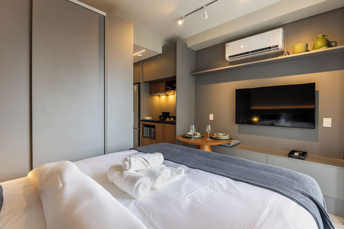Une chambre d’hôtel moderne dotée d’un grand lit, d’un téléviseur à écran plat fixé au mur, d’un petit coin cuisine et d’un appareil de climatisation.
