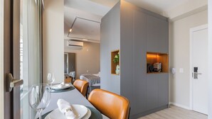 A dining area with a table set for two, a chair, and a small shelf with a plant. - Stay Home Luxo Itaim (São Paulo)