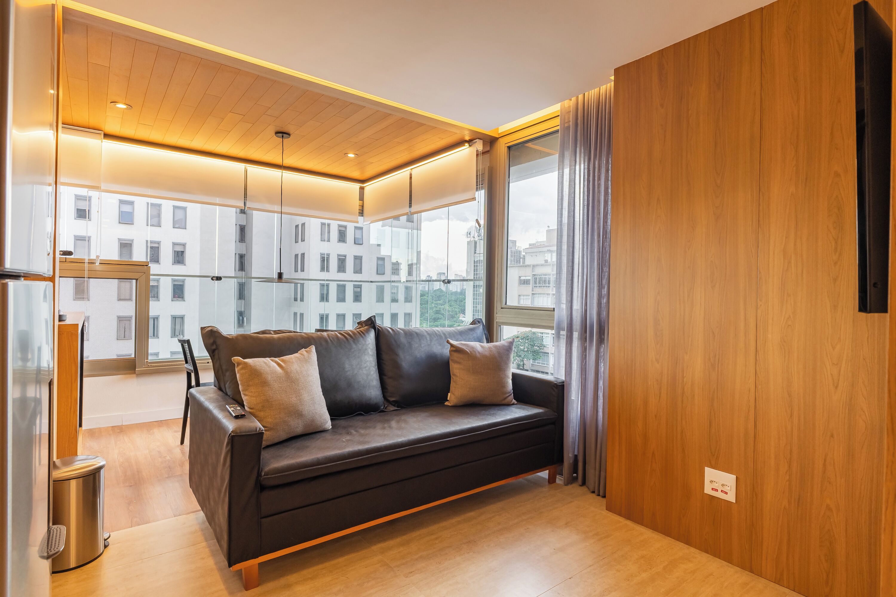 Una sala de estar moderna con un sofá oscuro, una pared de vidrio y vistas a edificios.